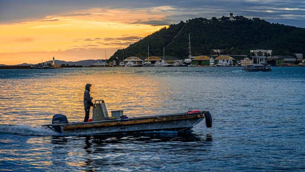 Person driving a small boat on the water at sunset.